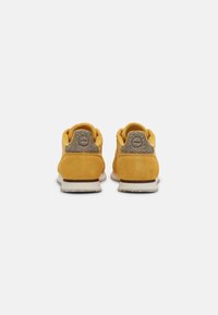 Gule ruskindsneakers med en tekstureret grå bagpanel, hvid sål og brun accent. Har en rund logo ved hælen.