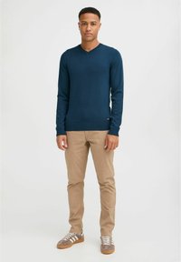 Tumed sinise värvi kudumiga kootud sviiter V-kaelusega, koos beežide pükstega ja pruunide tossudega, millel on valged triibud.