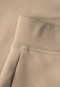 Nahaufnahme von beige geripptem Stoff, der eine gefaltete Kante mit feinen Nähdetails zeigt und die glatte Textur sowie das weiche Erscheinungsbild hervorhebt.