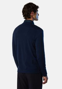 Pullover in maglina blu navy con colletto, polsini e orlo a coste. Tessuto liscio con fessure laterali per una maggiore libertà di movimento. Design minimale.