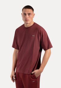 Bordeaux kleurige t-shirt met korte mouwen, gemaakt van katoen, met een ronde hals en een klein logopatch op de linker borst. Soepele textuur.