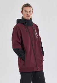 Bordeaux kleurige zip-up jas met zwarte mouwen en capuchon. Voorzien van trekkoorden, logo aan de voorkant en zijrits zakken. Gladde, gestructureerde stof.