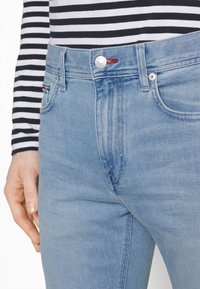 Ljusblå denimjeans med hög midja, med silverknapp och en röd detalj. Texturerat tyg med lätt urblekning.