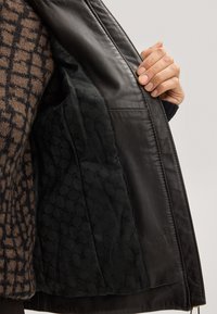 Schwarze Lederjacke mit einem gesteppten schwarzen Innenfutter mit dezentem Muster. Das Außenmaterial ist glatt, während das Futter Textur hinzufügt.