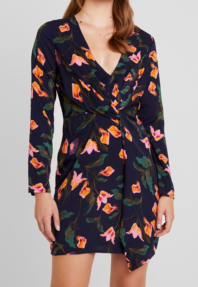 Sukienka w kwiaty z dekoltem w serek, długimi rękawami i granatowym tłem z żywymi różowymi i zielonymi wzorami kwiatowymi.