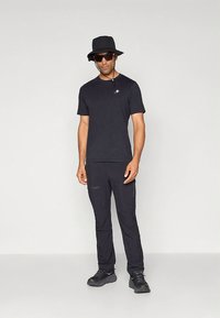 Juoda trumpomis rankovėmis marškinėliai ir ilgos kelnės, pagamintos iš lengvos medžiagos. Aksesuarai: juoda kibiro formos skrybėlė ir akiniai nuo saulės. Juodi batai.