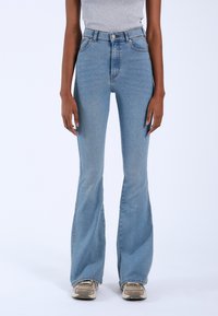 High-waisted light blue flared jeans in denim fabric with subtle stitching details and a smooth texture, paired with neutral sneakers.