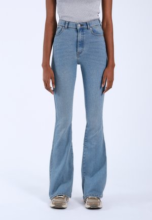 High-waisted light blue flared jeans in denim fabric with subtle stitching details and a smooth texture, paired with neutral sneakers.