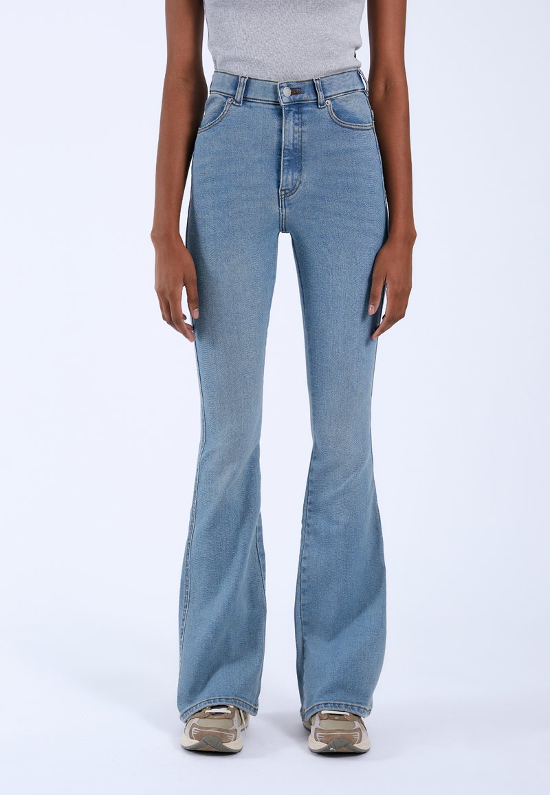High-waisted light blue flared jeans in denim fabric with subtle stitching details and a smooth texture, paired with neutral sneakers.