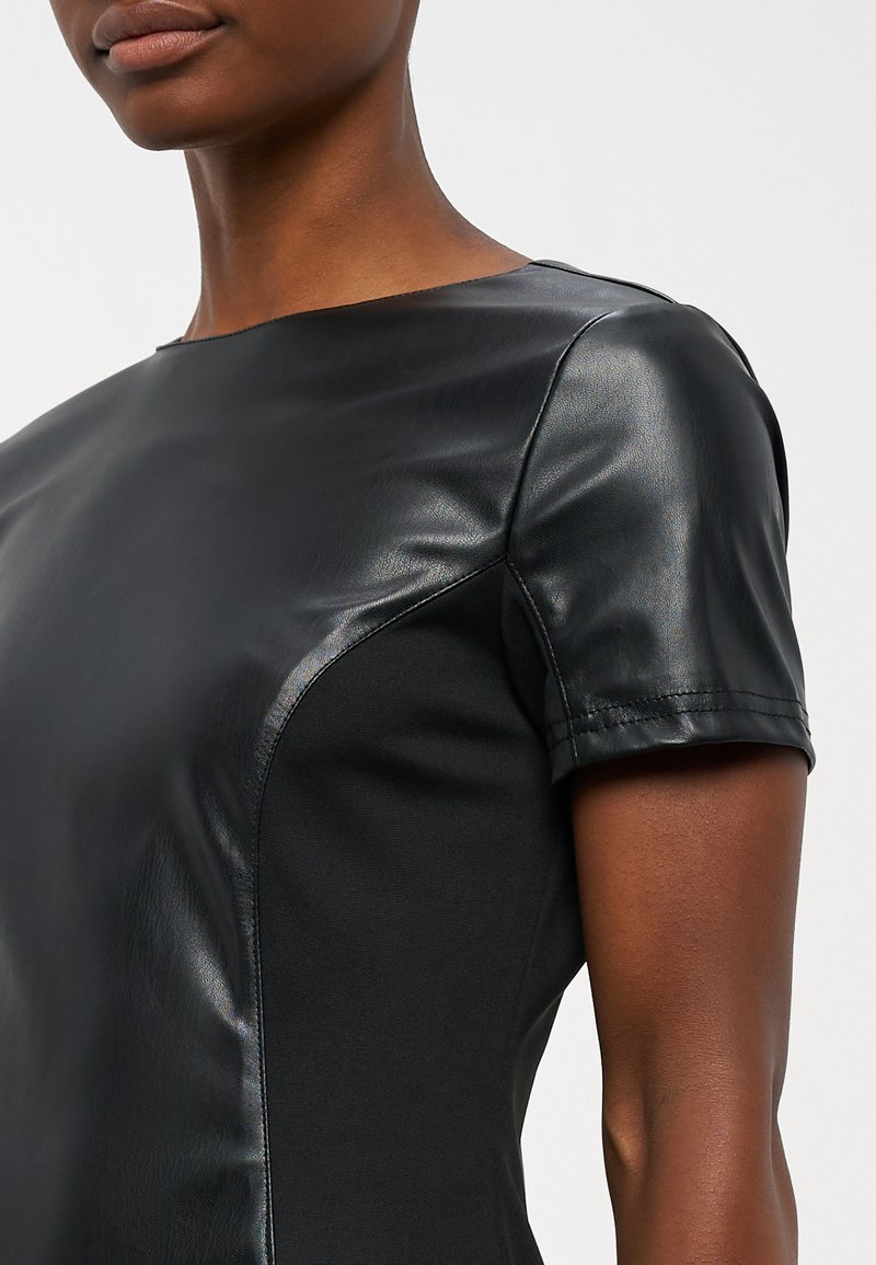 Schwarzes Kleid mit kurzen, glänzenden Lederärmeln und einem glatten, matten Körper. Schlankes Design mit kontrastierenden Texturen und klaren Linien.