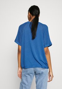 Modré pletené oversized tričko s krátkými rukávy, texturovanou látkou a volným střihem, doplněné světle modrými denimovými džínami.