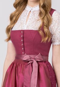Traditional dress featuring a maroon bodice with buttons, lace sleeves, and a satin bow at the waist, complemented by a flowing skirt.