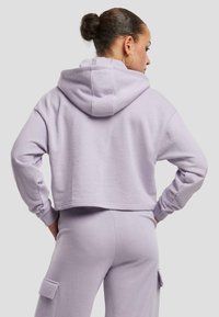 Hoodie lavanda cropped con cappuccio regolabile, maniche lunghe e polsini a coste, abbinato a pantaloni della tuta coordinati con tasche laterali.