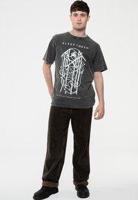 Dark gray cotton t-shirt featuring a white graphic print with intricate lines and text, paired with brown corduroy pants and black shoes.