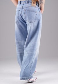 Helle blaue Denim-Jeans mit lockerer Passform, fünf Taschen und einem Lederpatch am hinteren Bund. Mit Ausbleichungen an den Beinen und umgeschlagenen Säumen.