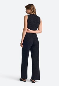 Must mustriga, ilma varrukat hüppaülikond, millel on jalga ulatuvad püksid ja ühendatud ülemine osa. Valmistatud tekstuurses kangas, millel on peen kuma. Sellel on selja lukuga sulgemine.