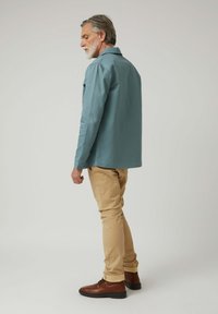 Camisa de algodón azul claro con cuello, combinada con pantalones beige. Botas marrones con cordones completan el conjunto. Diseño limpio y sencillo con un ajuste relajado.