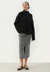 Schwarzer gerippter Strickrollkragenpullover mit langen Ärmeln, kombiniert mit einem grauen Jeansrock mit einem Schlitz vorne und schwarzen Ballerinas.