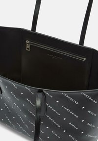Borsa tote nera con una texture liscia, stampata con testo e loghi del marchio bianchi. Include una tasca interna con cerniera e manici neri.