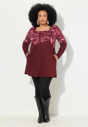 Tunique bordeaux avec un motif paisley rose en haut, à manches longues et poches, associée à des leggings noirs et des bottes de cow-boy noires.