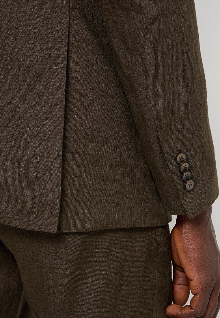 Braune Leinenanzugsjacke mit ausgeprägter Textur, ausgestattet mit einem einzelnen Schlitz, vier abgerundeten Knöpfen am Ärmel und maßgeschneiderten Details.