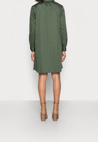 Grön långärmad klänning med krage, slät textur och knälång design. Buren med beige ankelstövlar med klack.