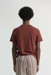 Camiseta corta de manga en color marrón con escote redondo y ajuste relajado, combinada con pantalones estampados que presentan rayas verticales en varios colores.