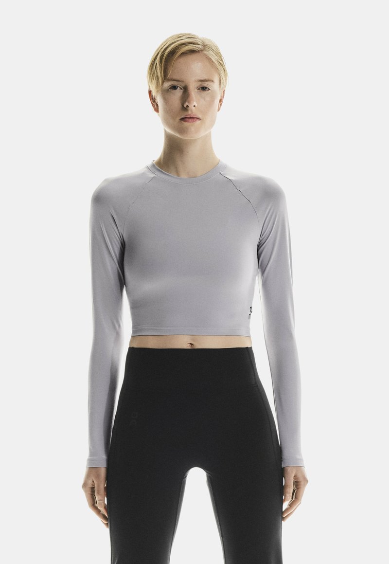 Hellgrauer, langärmliger Crop-Top aus dehnbarem Stoff mit rundem Ausschnitt und schlankem Design. Kombiniert mit hoch taillierten schwarzen Leggings.