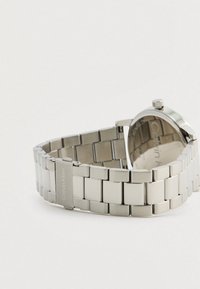 Ασημένιο ρολόι από ανοξείδωτο ατσάλι με σχέδιο συνδεδεμένης βραχιόλι, στρογγυλή θήκη και λεπτομέρεια στη κορώνα. "Calvin Klein" χαραγμένο στην πόρπη.