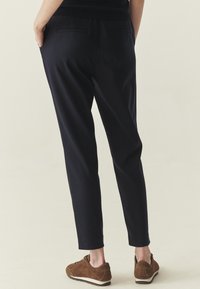 Pantalon bleu marine à coupe fuselée, doté d'une texture douce et de poches latérales. Associé à des baskets en daim marron.