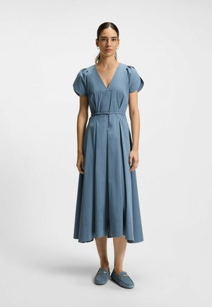 Hellblaues Kleid mit kurzen Puffärmeln, V-Ausschnitt, taillierter Taille und ausgestellt Rock. Kombiniert mit blauen Slippers, vor einem schlichten Hintergrund.