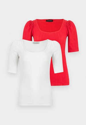 Hauts en maille côtelée blanche et rouge avec encolures carrées et manches bouffantes mi-longues, superposés sur un fond clair uni.
