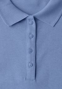 Polo en maille bleu clair avec un col et quatre boutons assortis sur la patte de boutonnage, montré en gros plan.