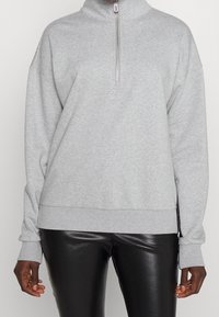 Felpa grigia con zip e colletto alto, dal fit rilassato, con polsini e orlo a costine. Realizzata in materiale morbido con una sottile trama. Abbinata a leggings neri.