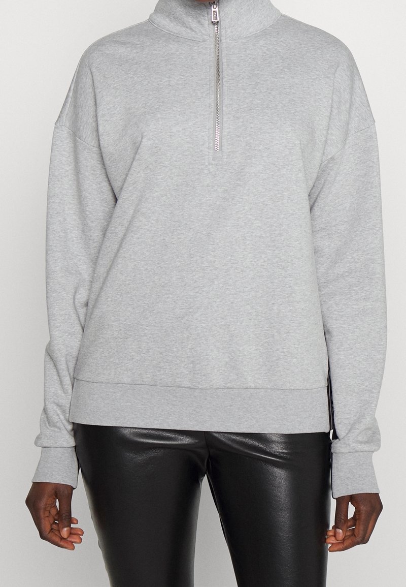 Felpa grigia con zip e colletto alto, dal fit rilassato, con polsini e orlo a costine. Realizzata in materiale morbido con una sottile trama. Abbinata a leggings neri.
