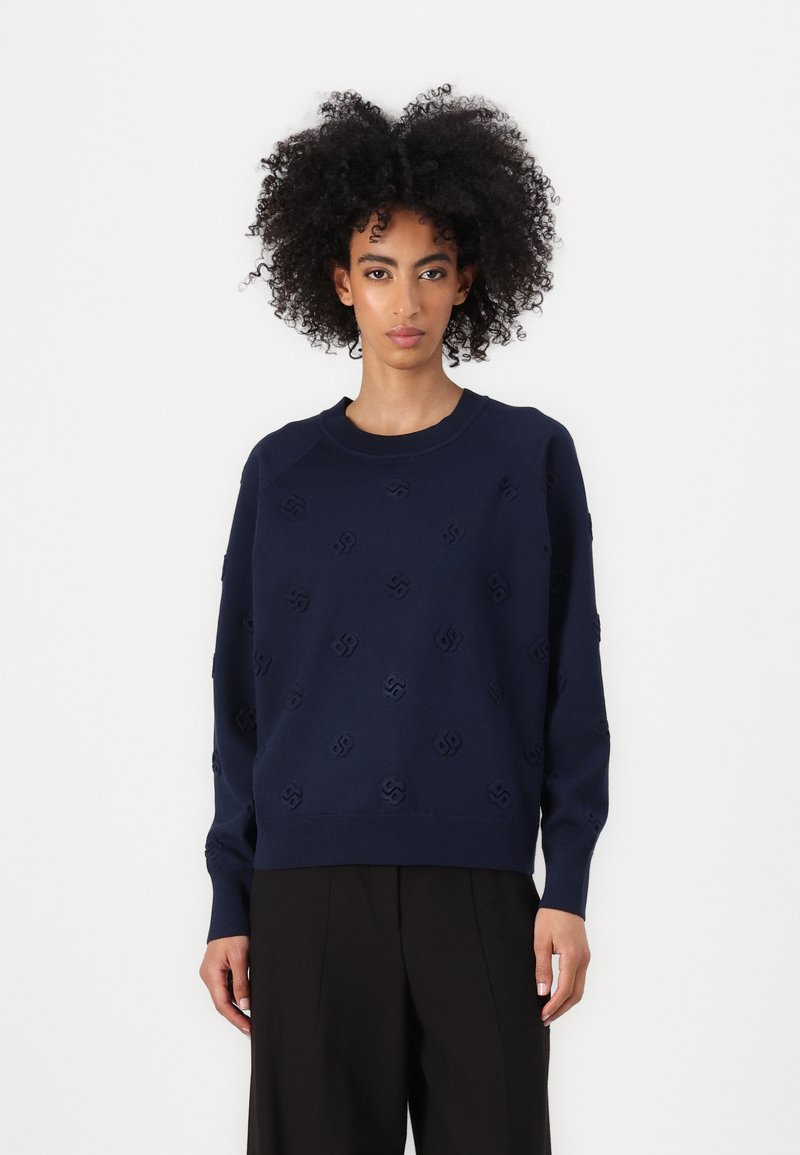 Mørkeblå strikkegenser med strukturmønster, rund hals, senkede skuldre og ribbestrikkede ermer og fald. Glatt overflate, avslappet passform.