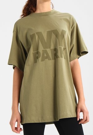Olive zielona, oversize'owa koszulka z bawełny, z wyraźnym logo „IVY PARK” w ciemniejszym odcieniu, krótkimi rękawami i okrągłym dekoltem.