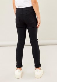 Jeans skinny noirs avec une taille haute, deux poches arrière et des manches retroussées, associés à des baskets blanches.