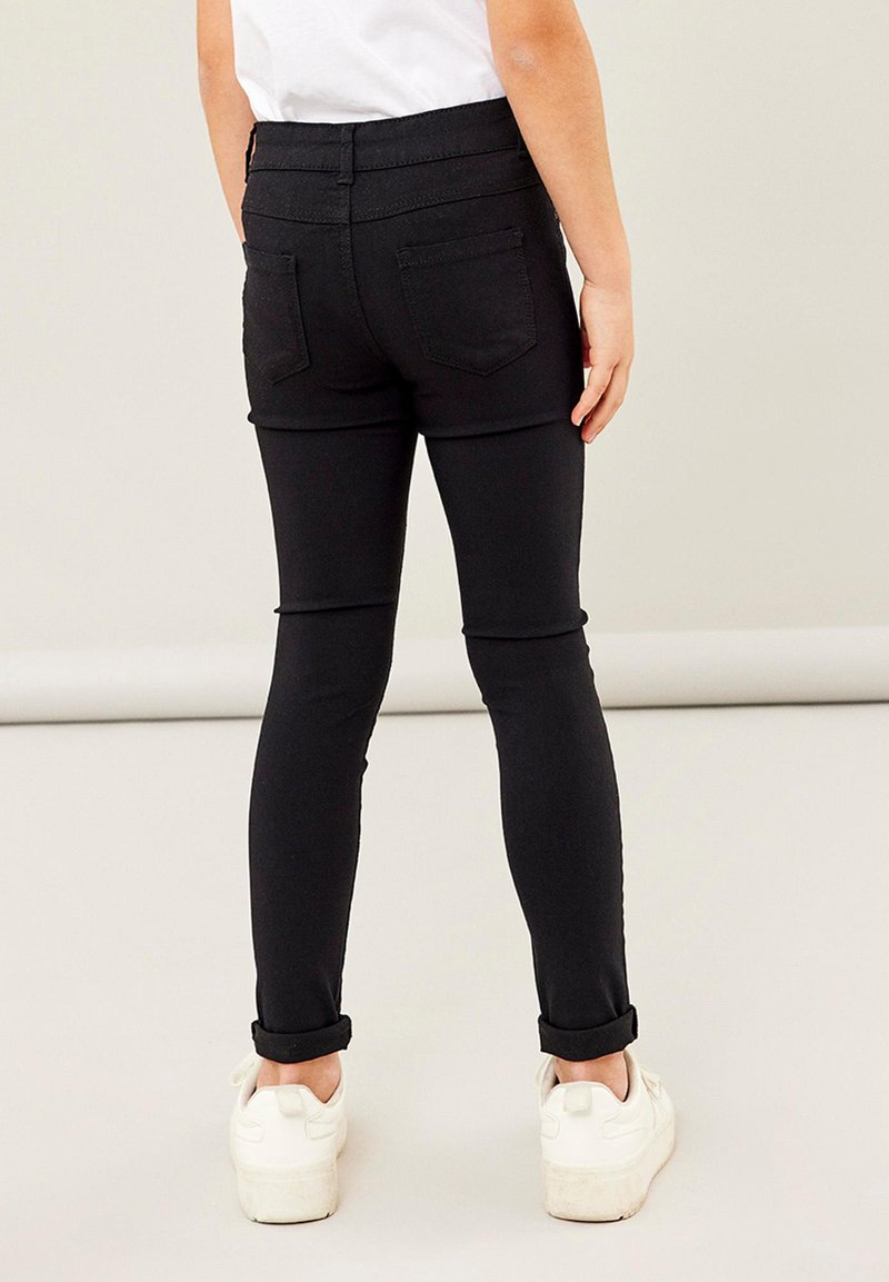 Jeans skinny noirs avec une taille haute, deux poches arrière et des manches retroussées, associés à des baskets blanches.