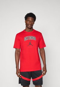 Červené bavlněné tričko s nápisem "CHICAGO" a černým logem Jordan uprostřed, doplněné černými šortkami s červenými akcenty.