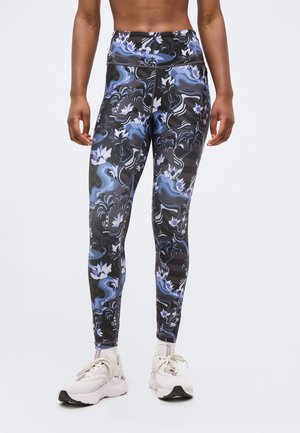 Kõrge vöökohaga retuusid abstraktse musta, sinise ja lilla lillemustriga, mida kannab seisval inimesel valgete tossudega.