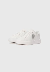 Pair of white low-top sneakers with white laces and a silver embroidered shield logo on the outer side against a plain background.