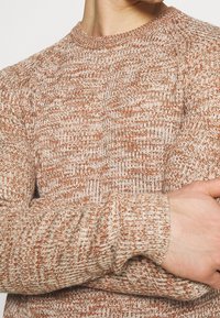 Brun och krämfärgad texturerad stickad tröja med rund halsringning och långa ärmar, som har ett blandat mönster och ribbade ärmslut.