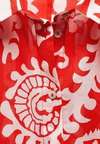 Rood-wit gebloemd overhemd met witte knopen en een omgeslagen kraag, met close-up details van de stof en het stiksel.