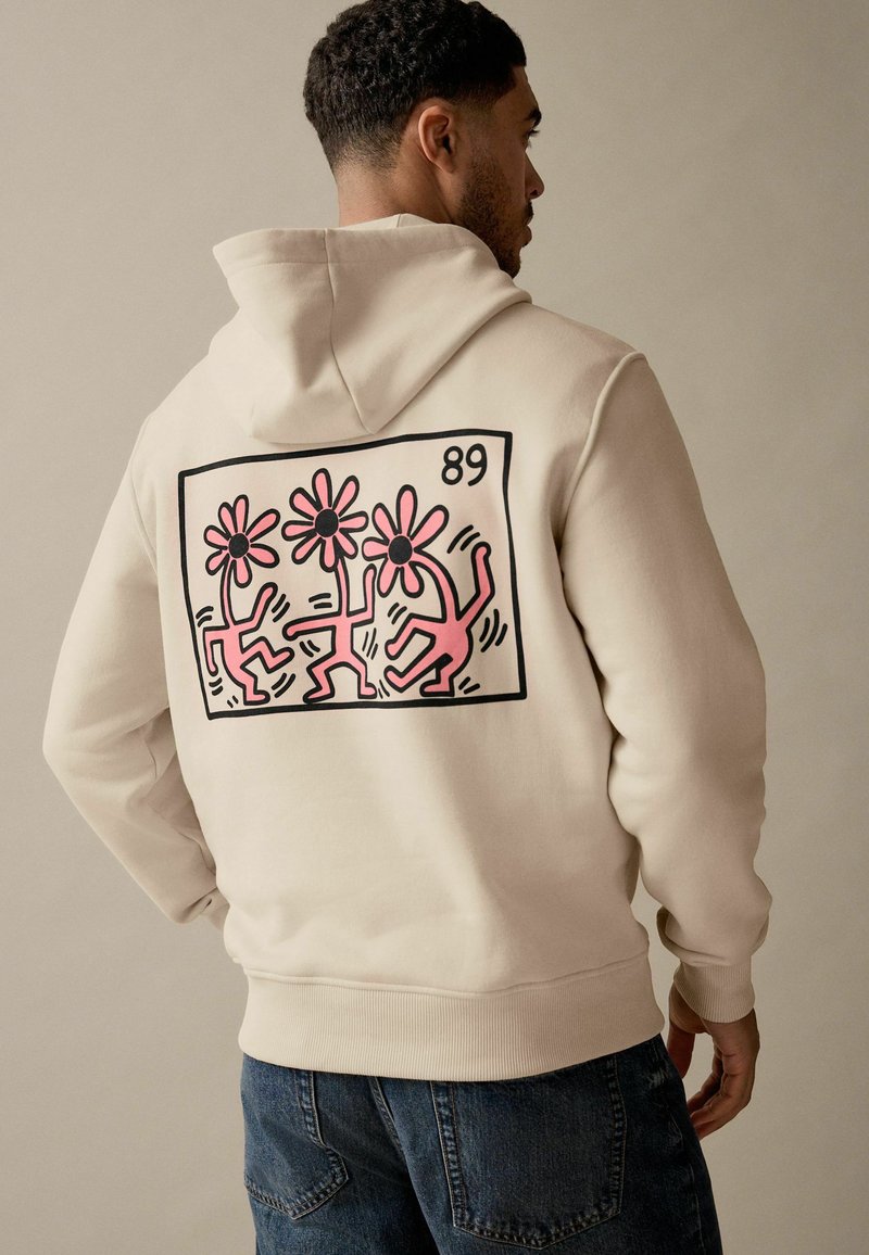 Beżowa bluza z kapturem z dużą grafiką na plecach przedstawiającą trzy różowe kwiaty i abstrakcyjne figury w czarnym obrysie, numer stylu 89. Miękka tkanina, luźny krój.