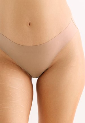 Nahaufnahme des unteren Bauchs und der oberen Oberschenkel einer Person, die nahtlose, hautfarbene Unterwäsche trägt, mit sichtbaren Dehnungsstreifen am linken Oberschenkel.