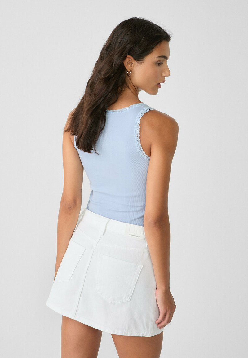 Débardeur côtelé bleu clair avec bord en dentelle, associé à une mini-jupe en denim blanche avec deux poches arrière et une texture lisse.