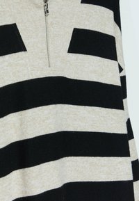 Pullover a righe nere e beige con colletto zip, realizzato in un materiale morbido e texture. Presenta audaci righe orizzontali.