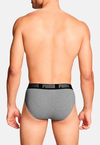 Graue Baumwollunterhosen mit einem schwarzen Bund, auf dem das eingravierte "PUMA"-Logo zu sehen ist. Die Rückansicht zeigt eine enge Passform und eine glatte Textur.