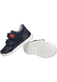 Scarpe in pelle blu navy con due cinturini in Velcro, suola in gomma bianca e fondo testurizzato per una migliore presa. Accent nel colore rosso sul cinturino.